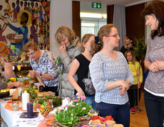 Ein langer Verkaufstisch mit diversen Blumen, Kerzen und einer Frau, die verkauft. Zahlreiche Leute sind daran interessiert.