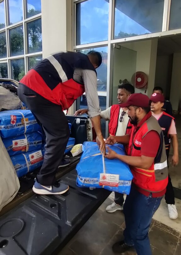 Mitarbeitende von Caritas Nepal laden verpackte Hilfsgüter von einem Geländewagen für die Fluthilfe ab.