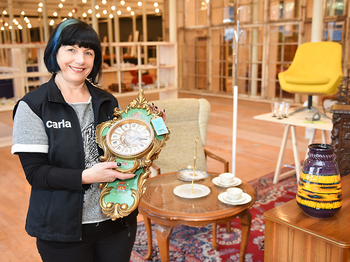 Carla Mitarbeiterin steht vor dekoriertem Tisch mit antiker Uhr im carla Store Bludenz.