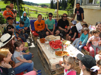 Viele Menschen sitzen im Freien auf selbstgemachten Holzpaletten Sofas. in der Mitte befindet sich ein Holztisch mit verschiedenen Häppchen.