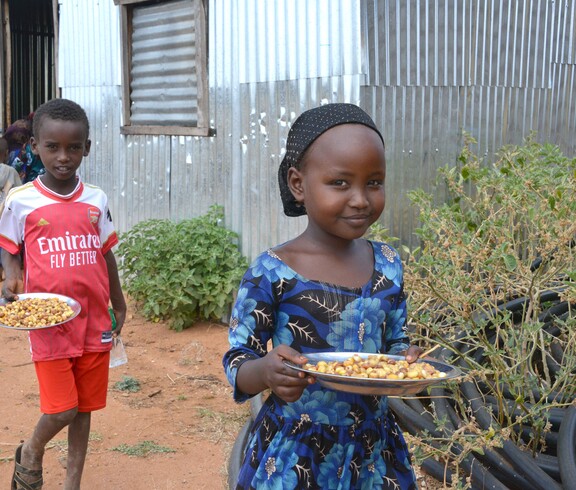 Ein Mädchen und ein Junge mit Tellern voller Mais und Bohnen stehen vor einem Schulgebäude in Borana.
