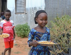 Ein Mädchen und ein Junge mit Tellern voller Mais und Bohnen stehen vor einem Schulgebäude in Borana.