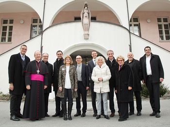 Eine Gruppe Erwachsener, unter anderem Bischof Benno Elbs vor dem Hospiz am See Gebäude.
