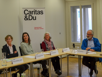 Sozialpaten sitzen an einem Tisch und hören dem Caritas Direktor zu.