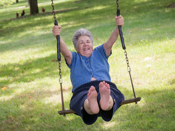 A senior woman relives her childhood memories as she joyfully swings on a rustic swing at the edge of a country walnut orchard. A,Senior,Woman,Relives,Her,Childhood,Memories,As,She,Joyfully