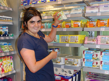 Bianca Panek, eine junge erwachsene Frau mit schwarzen langen Haaren und einem dunkelblauen t-Shirt, ist gerade am Einräumen von Waaren in einem Drogeriemarkt. 