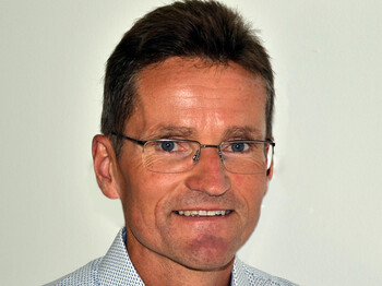 Bernd Klisch strahlt für ein Personalfoto. Er trägt ein hellblaues Hemd, eine Brille und hat kurze dunkle Haare.