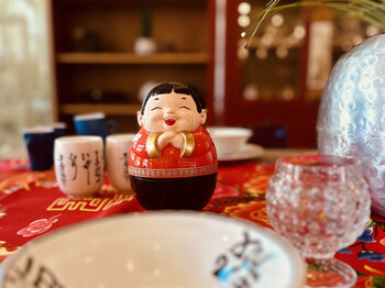Eine freundliche asiatische Figur steht inmitten von exotischem Geschirr auf einem fein gedeckten Tisch im carla Store Bludenz.