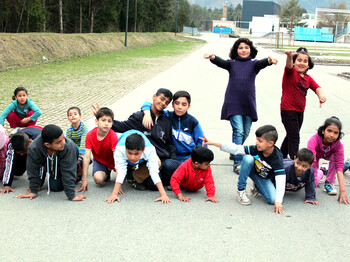 Viele Flüchtlingskinder versammeln sich im Freien für ein Lauftraining. Sie tragen Sportkleidung und sind schon in Startposition.