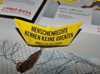 Gelbes Anmesty International Papierschiff zum Tag der Menschenrechte auf Schreibtisch