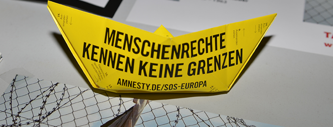 Gelbes Anmesty International Papierschiff zum Tag der Menschenrechte auf Schreibtisch