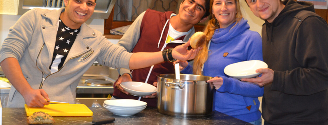 Vier junge Erwachsene kochen gemeinsam in einer kleinen Küche. 