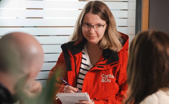 Frau mit Brille und roter Jacke von Carita & Du schreibt in Notizbuch