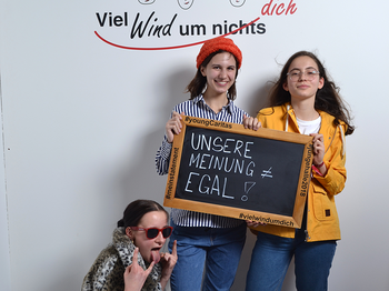 Drei Mädchen stehen mit einem Schild vor der Kamera