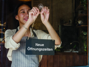 Young Asia manager girl changing a sign from closed to open sign on door cafe looking outside waiting for clients after lockdown. Owner small business, food and drink, business reopen again concept. Young,Asia,Manager,Girl,Changing,A,Sign,From,Closed,To