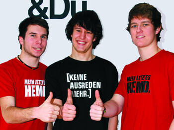 Zwei junge Männer mit einem roten T-Shirt und ein junger Mann mit einem schwarzen T-Shirt zeigen mit dem Finger "Thumbs up".