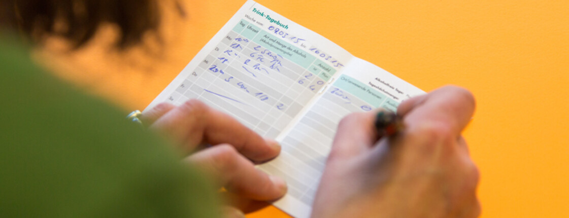 eine Frau, die von hinten gezeigt wird, notiert etwas in einen kleinen Kalender.