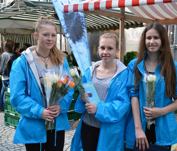 Drei junge Mädchen beim Verkauf von bunten Rosen für einen guten Zweck.