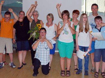 Menschen mit Beeinträchtigung und Betreuer stehen für ein großes Gruppenbild zusammen. Einige strecken ihre Arme dabei hoch. Der großteil ist weiß bekleidet. 