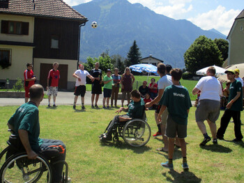 Mehrere Klienten der Werkstätten spielen auf einem grünen Rasen Fußball. Zwei von Ihnen sitzen dabei in ihrem Rollstuhl.