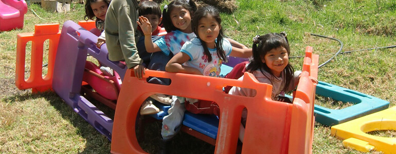Equadorianische Kinder sind auf einer grünen Wiese im Freien am Spielen. Sie strahlen große Freude dabei aus. 