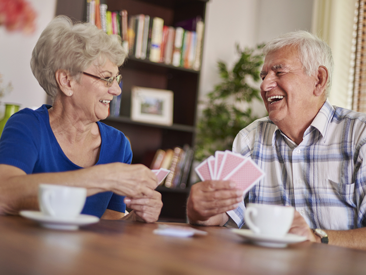 Zwei SeniorInnen amüsieren sich beim Kartenspielen und Kaffeetrinken.