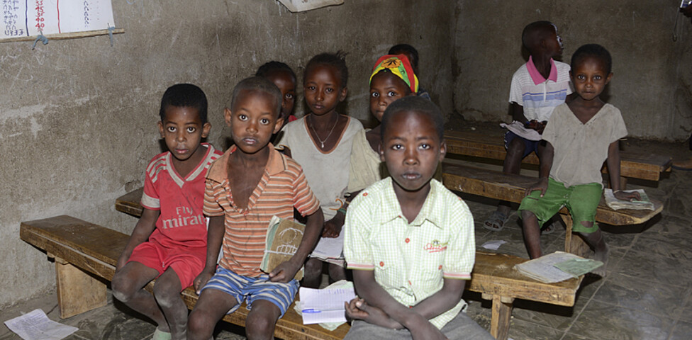 Äthiopische Straßenkinder in einer Schule in einem schlecht ausgeleuchteten Kassenzimmer. Sie sitzen auf provisorischen Schulbänken. Gekleidet sind sie schlicht in alten Klamotten. 