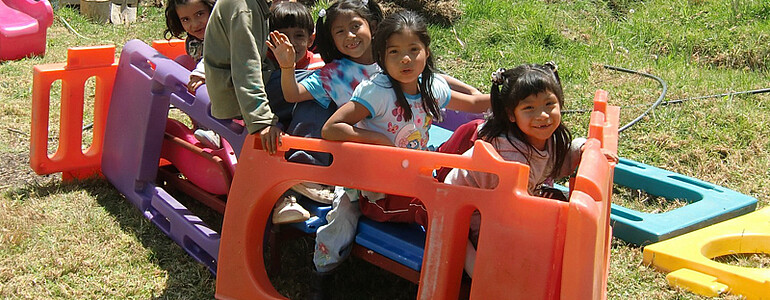 Equadorianische Kinder sind auf einer grünen Wiese im Freien am Spielen. Sie strahlen große Freude dabei aus. 