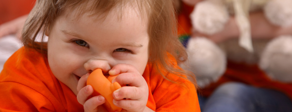 Baby mit braunen Haaren und orangem T-shirt vor Kleinkind mit Teddybär
