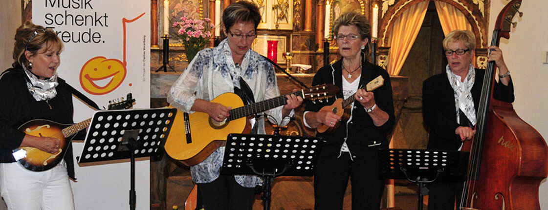 Eine Gruppe aus älteren Damen spielt in einer Kirche Lieder. Alle vier sind modisch schlicht gekleidet. 