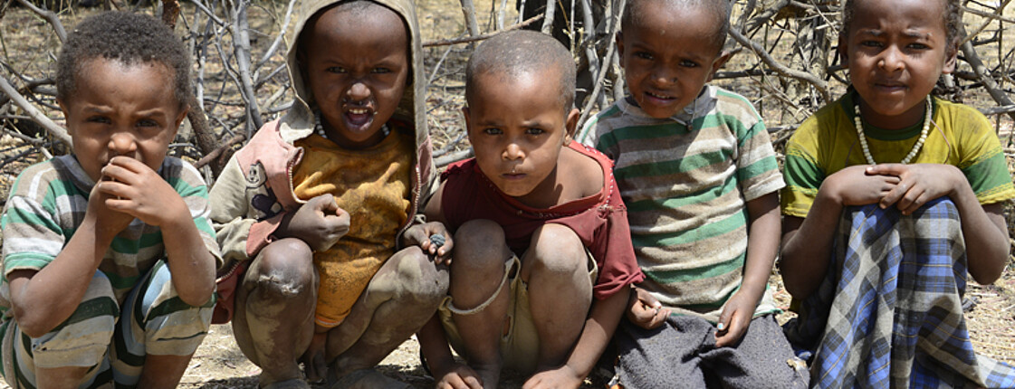 Fünf äthiopische Straßenkinder sitzen auf dem Boden. Sie sind im Freien und tragen altes, zerzaustes Gewand. 